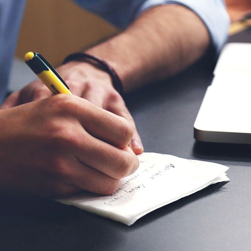 Close up the hands of a man writing on note paper with a pencil