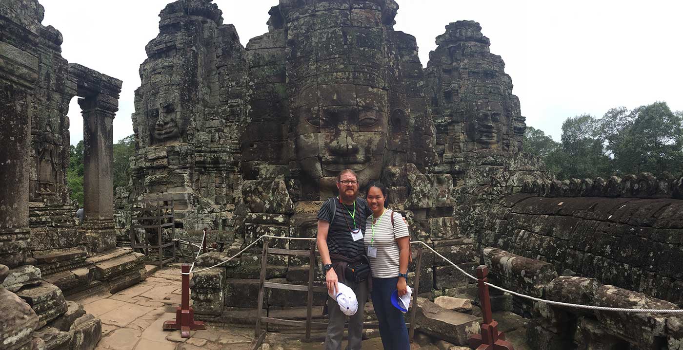 A couple arm in arm standing in the ruins of Ankor Thom.